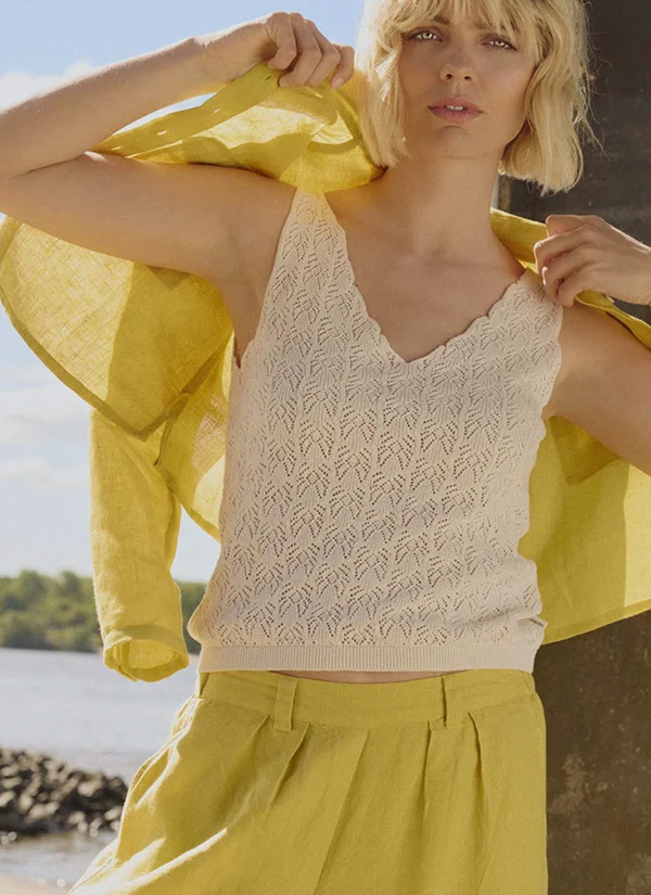 Model met crèmekleurige gebreid hemdje en gele linnen zomerbroek voor de merk pagina over Tranquillo