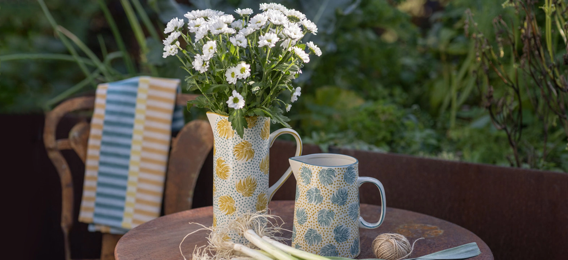 Een vaas gevuld met bloemen en een karaf met water staan op een tuintafel